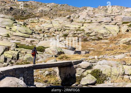 Escursioni turistiche maschili su un ponte di pietra, sentiero fino al lago Laguna grande de Gredos dalla Plataforma de Gredos nelle montagne della Sierra de Gredos, Spagna. Foto Stock