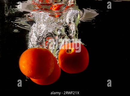 Pomodoro maturo cade profondamente sotto l'acqua con un grande splash. Foto Stock