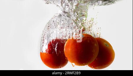 Pomodoro maturo cade profondamente sotto l'acqua con un grande splash. Foto Stock