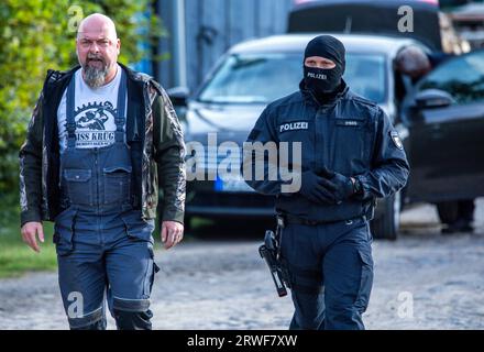 Jamel, Germania. 19 settembre 2023. Sven Krüger (l), un estremista di destra conosciuto in tutta la Germania, è accompagnato da un agente di polizia durante un'operazione di ricerca sulla sua proprietà. Il ministro federale degli interni Faeser ha vietato l'associazione estremista di destra "Hammerskins Germany”, le sue propaggini regionali e la sottoorganizzazione "Crew 38”. Secondo il ministero, le forze di polizia hanno perquisito le case di 28 sospetti membri dell'associazione in dieci stati tedeschi la mattina presto. Credito: Jens Büttner/dpa/Alamy Live News Foto Stock