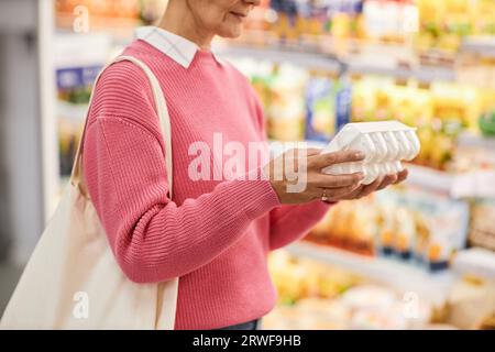 Primo piano della vista laterale di una donna adulta che tiene una scatola di uova nel supermercato e controlla la data di scadenza, spazio copia Foto Stock