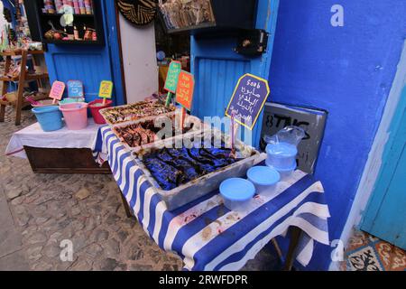 Una vivace e colorata scena del souk Chefchaouen con sapone nero marocchino in vassoi su un panno a righe blu e bianco e altri souvenir in vendita Foto Stock