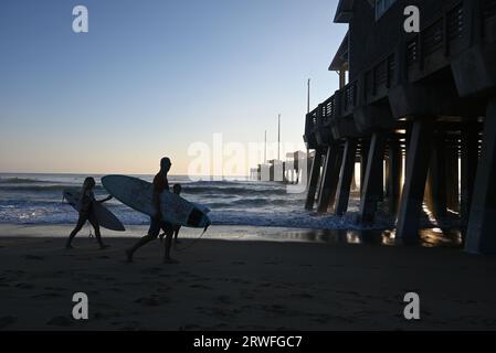 I surfisti portano le loro tavole lungo la spiaggia durante una mattinata di surf al largo del molo di Jennette a Nags Head, North Carolina. Foto Stock