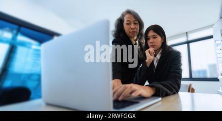 Mentore, coaching o donna d'affari con notebook, parla o pianifica un progetto in ufficio. Tecnologia, collaborazione di squadra, senior manager, spiegazione Foto Stock