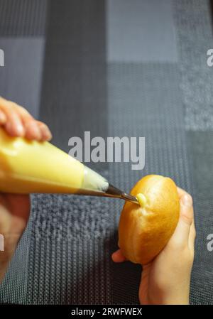 Mani che riempiono Krapfen con crema di vaniglia. Dessert dalla Germania come impasto di ciambelle Foto Stock