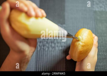 Mani che riempiono Krapfen con crema di vaniglia. Dessert dalla Germania come impasto di ciambelle Foto Stock