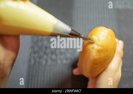 Mani che riempiono Krapfen con crema di vaniglia. Dessert dalla Germania come impasto di ciambelle Foto Stock