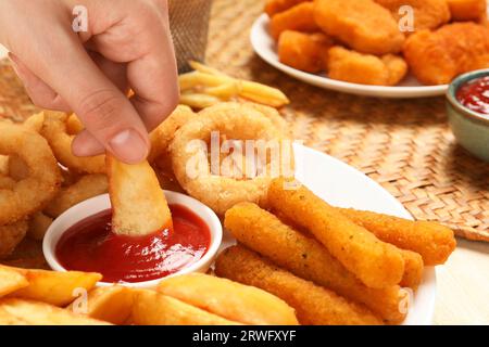 Donna che immerge le patate al forno nel recipiente con il saporito ketchup al tavolo, primo piano Foto Stock