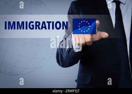 Immigrazione. Uomo d'affari che tocca lo schermo digitale con la parola e la bandiera dell'Europa su sfondo grigio, primo piano Foto Stock
