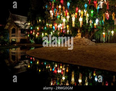 Lanterne colorate sopra la statua del Buddha. Decorazioni del festival di Loy Krathong e una piccola statua di Budhha vicino al fiume. Statua del Buddha d'oro sotto un bodhi tre Foto Stock