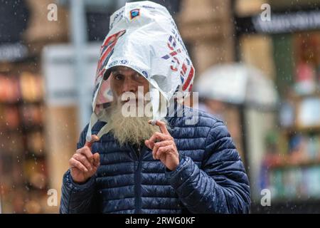 Uomo barbuto con borsa Tesco a vita sopra la testa a Preston, Lancashire. Meteo Regno Unito 19 settembre 2023. Negozi, amanti dello shopping in una giornata ventosa e piena di docce a Preston. Rimanendo ventoso, con galee locali a ovest. Questo pomeriggio sono attesi incantesimi di pioggia pesante e persistente. Credito. MediaWorldImages/AlamyLiveNews Foto Stock