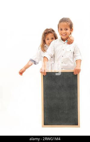 Inglese: Due bambini multietnici con i capelli lunghi tengono in mano una lavagna bianca su sfondo bianco Foto Stock