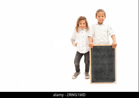 Inglese: Due bambini multietnici con i capelli lunghi tengono in mano una lavagna bianca su sfondo bianco Foto Stock