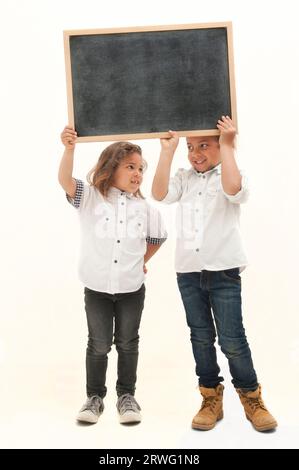 Inglese: Due bambini multietnici con i capelli lunghi tengono in mano una lavagna bianca su sfondo bianco Foto Stock