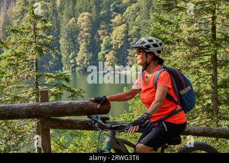 Bella donna anziana in mountain bike elettrica sul lago Feldsee sotto la vetta di Feldberg, Foresta Nera, Germania Foto Stock