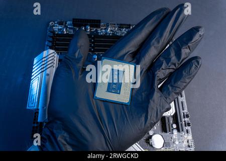 La mano con i guanti del tecnico tiene il chip della CPU sullo sfondo della scheda madre. apparecchiature informatiche. microelettronica hardware high-tech Foto Stock