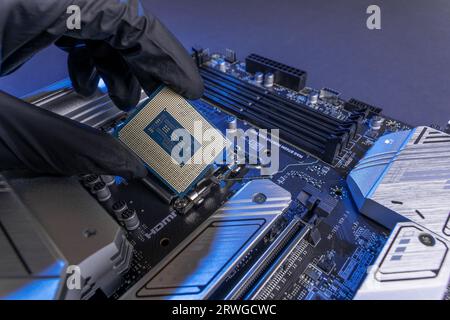 La mano con i guanti del tecnico tiene il chip della CPU sullo sfondo della scheda madre. apparecchiature informatiche. microelettronica hardware high-tech Foto Stock