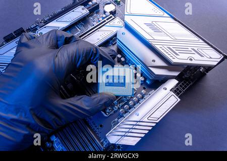 La mano con i guanti del tecnico tiene il chip della CPU sullo sfondo della scheda madre. apparecchiature informatiche. microelettronica hardware high-tech Foto Stock