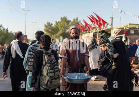 Un uomo iracheno distribuisce acqua tra i pellegrini musulmani sciiti che marciano da Najaf verso la città sacra di Karbala. Ogni anno milioni di musulmani sciiti e alcuni di altre fedi intraprendono un pellegrinaggio di 20 giorni a piedi da varie città dell'Iraq e dell'Iran verso la città Santa di Karbala. Questo pellegrinaggio è in memoria dell'Imam Hussein, nipote del profeta Maometto, morto in battaglia nel 680 d.C. Il 40° giorno di lutto per Hussein, conosciuto come Arbaeen, i pellegrini convergono a Karbala per rendere omaggio al suo santuario. Lungo la strada, i volontari forniscono cibo, acqua e riparo, e gli abitanti del villaggio aprono il loro Foto Stock