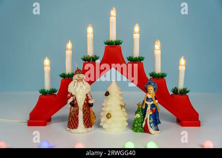 Babbo Natale, la fanciulla delle nevi e l'albero di Natale. Per festeggiare il nuovo anno, un candelabro natalizio con sette candele su sfondo blu invernale. Foto Stock