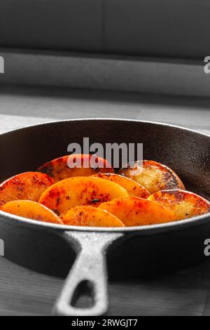 Mela fritta, varietà Pink Lady, in una padella in ghisa. Su un tagliere di legno in cucina. con colore selettivo Foto Stock