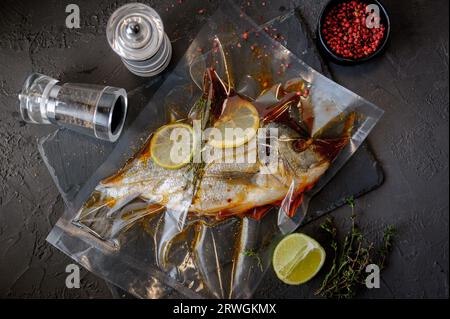 Pesce fresco dorado. dorado di pesce crudo con ingredienti speziati ed erbe aromatiche per cucinare su fondo di pietra nera. Vista dall'alto. Foto Stock