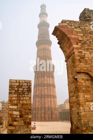 Qutb Minar la mattina di nebbia visto da all'interno di terreni storici e rovine fiancheggiate da alberi a Delhi, Inida. Foto Stock