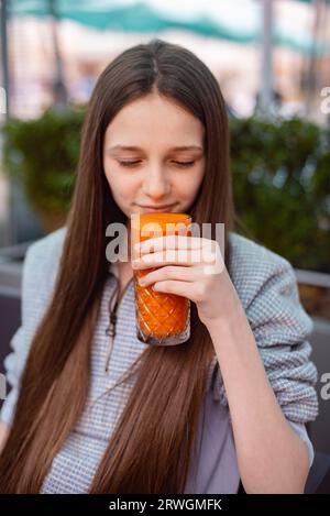 la ragazza adolescente apprezza e assaggia il succo fresco, bevendo frullato di zucca Foto Stock