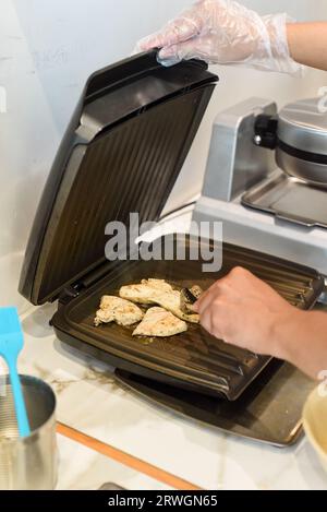 Cuoco che frigge la carne di pollo nel burro nella griglia elettrica Foto Stock