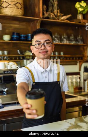 Cameriere vietnamita sorridente che tiene tazze di carta con caffè in un bar Foto Stock