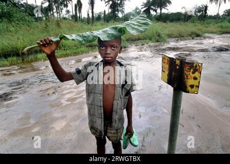 Nigeria: Un ragazzo si trova oltre a un segnale di pericolo da parte di una zona contaminata da petrolio a Ogoniland. Distruzione ambientale causata dalla fuoriuscita di petrolio greggio nella zona di produzione petrolifera del sud del paese, prevalentemente abitata dalla tribù Ogoni. Foto Stock