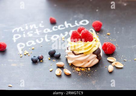 Primo piano della piccola torta pavlova al pistacchio con lamponi freschi e mirtilli su un lavagna di gesso nero Foto Stock