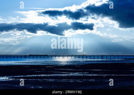 Una vista lontana del molo di Southend al crepuscolo con raggi di luce che si infrangono tra le nuvole. La marea è finita. Foto Stock