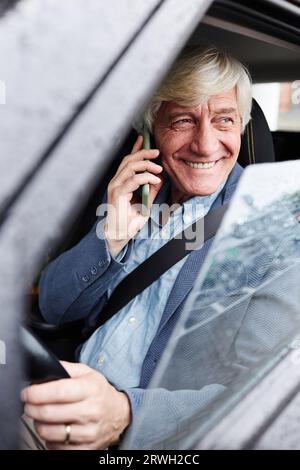 Ritratto verticale di un uomo anziano sorridente dai capelli bianchi che parla al telefono all'interno dell'auto Foto Stock
