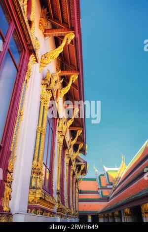 Un tempio thailandese con tetto rosso, accenti dorati e statue mitiche di creature, adagiato su un cielo blu. Foto Stock