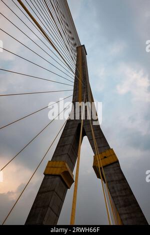 Un torreggiante ponte sospeso, con pilastri in cemento e cavi in acciaio, cielo nuvoloso. Foto Stock