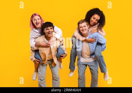 Spensieratamente eccitate coppie multirazziali che si divertono, graziose donne che fanno schifo i loro fidanzati su sfondo giallo Foto Stock