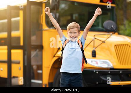 Ritorno a scuola. Happy Boy Jumping vicino a Shool Bus e alzando le mani Foto Stock