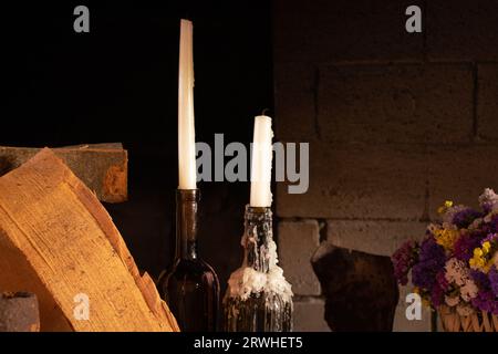 Due lunghe candele si stendono in bottiglie di vino sul tavolo accanto a un vaso di fiori secchi durante il giorno a casa, nell'arredamento e nelle vacanze Foto Stock