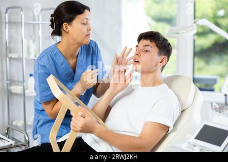 Giovane cosmetologa che esamina il volto di un giovane uomo Foto Stock
