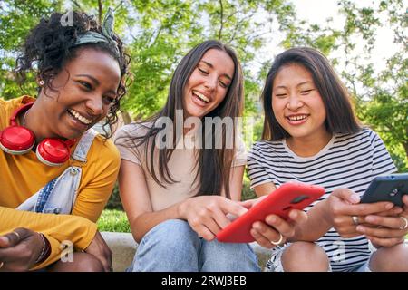 Tre donne felici che usano il cellulare all'aperto. I compagni di classe si divertono a guardare qualcosa sul cellulare. Foto Stock