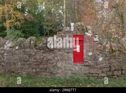 Shrewsbury, Shropshire, Regno Unito - 23 novembre 2022 - casella postale rossa britannica incastonata in un muro di mattoni frastagliati nella campagna dello Shropshire Foto Stock