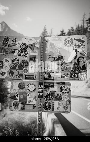 Una segnaletica stradale coperta da adesivi e decalcomanie. La Duffy Lake Road, tra Lillooet e Pemberton BC, Canada. Immagine in bianco e nero. Foto Stock