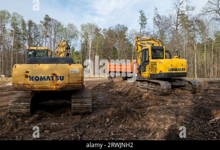 CROW WING CO, MN - 10 MAGGIO 2023: Due escavatori gialli Komatsu visti da dietro e un dumper arancione, in un nuovo cantiere edile. Foto Stock