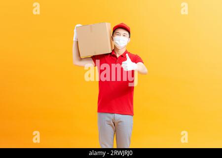 Giovane uomo asiatico che indossa maschera protettiva e guanti che dà cartone pacchi al cliente Foto Stock