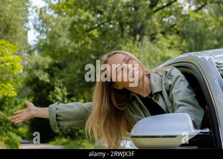 Donna bionda che esce dalla macchina del parabrezza. I giovani turisti esplorano i viaggi locali, trasformandoli in momenti autentici. Emozioni vere espressioni di fuga e di rinfrescarsi rilassarsi all'aria aperta e pulita Foto Stock