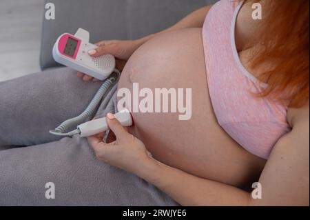 Primo piano della pancia di una donna incinta usando un doppler domestico. Schermo vuoto. Foto Stock