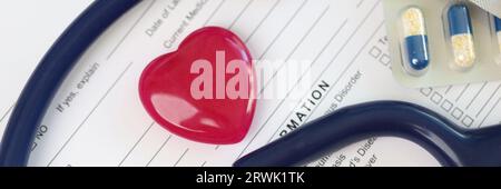 Cuore rosso, stetoscopio e pillole su foglio di storia medica del paziente forma. Foto Stock