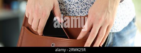 Donna in abiti casual tiene il suo smartphone nella sua borsa a spalla. Foto Stock