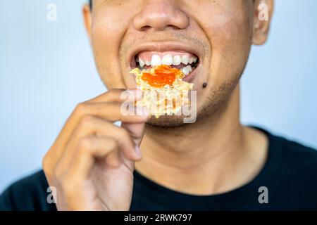 Uomo che mangia gorengan con sfondo bianco. Cibo tradizionale indonesiano Foto Stock